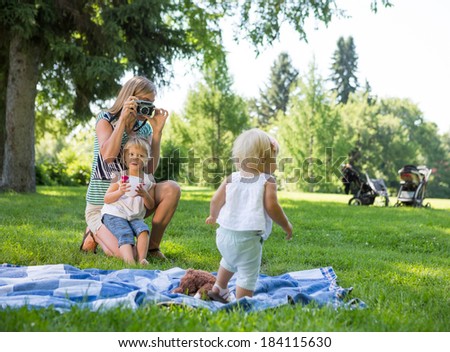 Mid adult mother photographing daughter during picnic in park