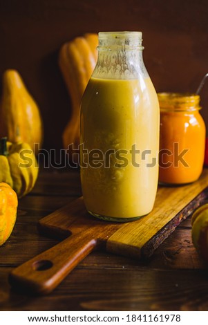 Pumkpin and tomato soup on a glass jar on a wooden cutter over a rusty background, and a butternut squash with a potatoes soup bottle in the back