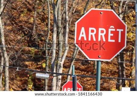 2 Stop signs in French translation of Stop in English, with colorful trees in autumn with black electricity cable
