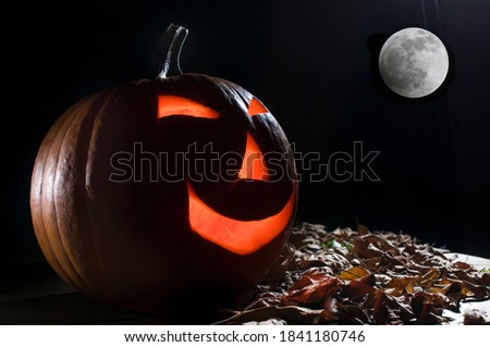 scary halloween pumpkin head, with a rim light at the back of the head and dry leaves on the side, with a full moon on the background, halloween party concept.