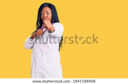 Young african american woman wearing doctor stethoscope punching fist to fight, aggressive and angry attack, threat and violence 