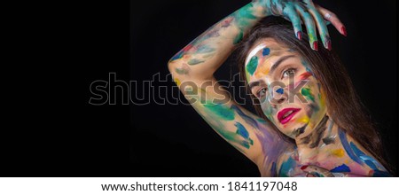 Beautiful and young girl with green eyes and face paint with multiple color in a black blackground.