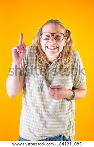 Studio photo of a very happy and geeky blonde girl with glasses on yellow background.