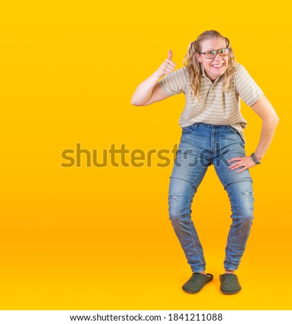 Studio photo of geeky blonde girl with glasses making thumbs up on yellow background.