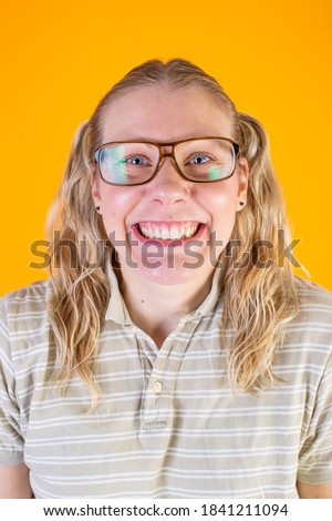 Studio photo of very happy and geeky blonde girl with glasses on yellow background.