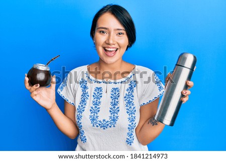 Beautiful young woman with short hair drinking mate infusion smiling and laughing hard out loud because funny crazy joke. 