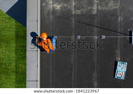 Caucasian Technician Wearing Orange Uniform and Hard Hat Installing Lightning Protection System Rod on Top of Commercial Building. Protect Structure From Elements.
