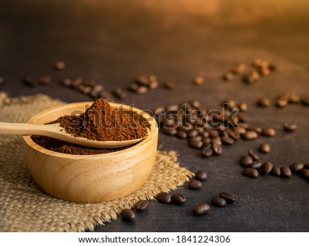 The picture of grated coffee in spoon on roasted coffee beans background.Wooden spoon with good quality coffee.
