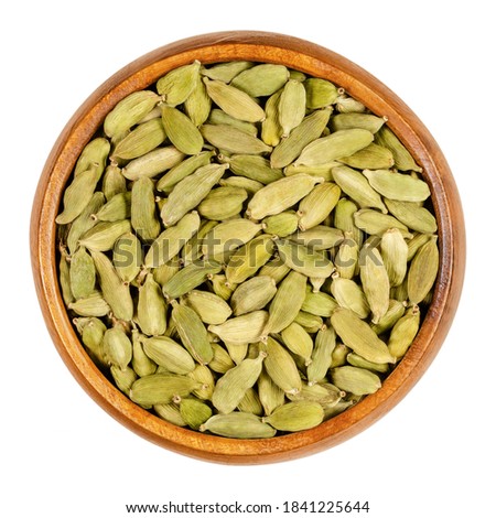Green cardamom pods in a wooden bowl. True cardamom, processed pods and seeds of Elettaria cardamomum, sometimes cardamon or cardamum, used as a spice. Close-up, from above, isolated macro food photo. Royalty-Free Stock Photo #1841225644