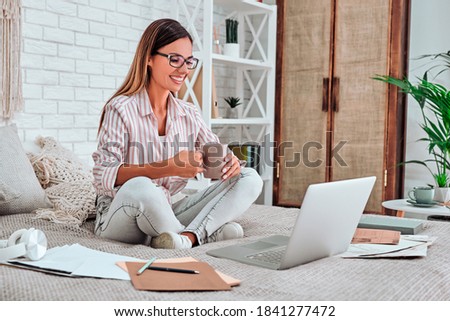 Happy casual beautiful woman working on a laptop sitting on the bed in the house. Copy space