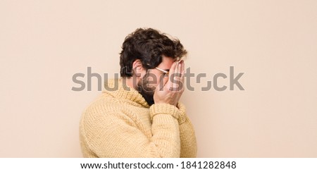 young cool man feeling sad, frustrated, nervous and depressed, covering face with both hands, crying against flat wall