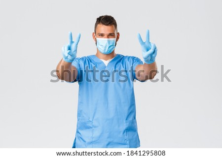 Healthcare workers, covid-19, coronavirus and preventing virus concept. Handsome hispanic doctor, nurse in scrubs and medical mask with gloves, show peace signs, stay positive