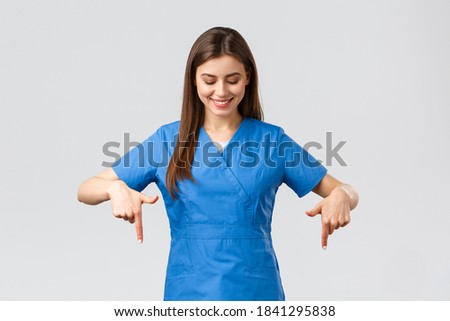 Healthcare workers, prevent virus, covid-19 test screening, medicine concept. Happy and pleased attractive female nurse or doctor, physician in blue scrubs, pointing looking down at advertisement