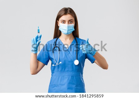 Covid-19, preventing virus, healthcare workers and quarantine concept. Confident female nurse, doctor in blue scrubs, medical mask and gloves assure in quality of coronavirus vaccine, hold syringe Royalty-Free Stock Photo #1841295859