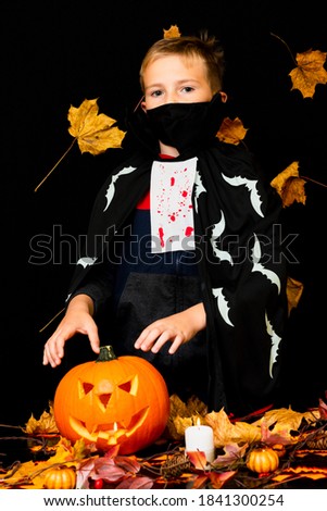 Young boy wearing face mask costume dressed as a halloween cosplay of scary dacula want to touch a jack'o pumpkin lantern on black yellow leaves background.Studio shot.