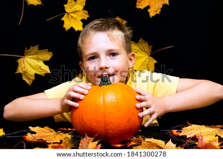 young boy child kid holding natural organic pumpkin in hands on a dark table with yellow maple leaves close up photos with smiling face