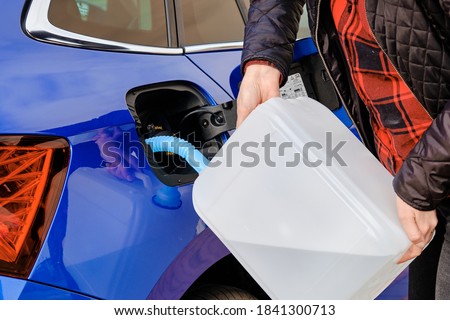 Woman filling a diesel engine fluid from canister into the tank of blue car. Diesel exhaust fluid for reduction of air pollution.  Royalty-Free Stock Photo #1841300713