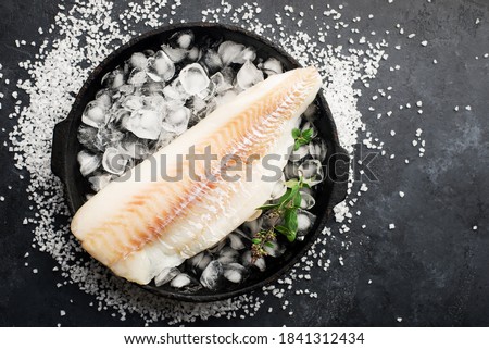Fillet of white sea cold-water fish cod in ice cubes on a dark background. Top view.