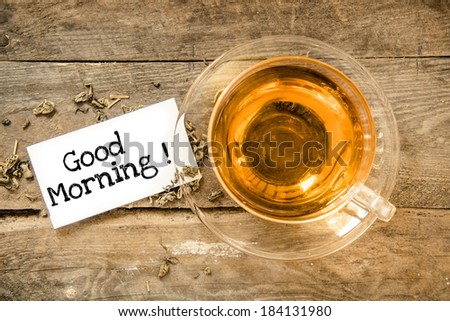 Cup of tea on table and paper sheet with text Good Morning