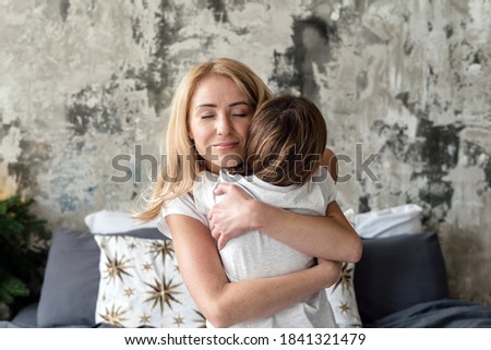 Cheerful and dreamy mother hugging her lovely daughter, spending lazy morning on weekend together with child at home. Concept of sincere and happy family