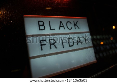Lightbox Sign Black Friday behind a glass window of the shop during the rain at night. Concept Black friday, season sales time.