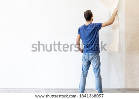 a man tears off old wallpaper from the wall during renovation, image with copy space