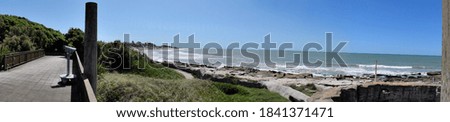 Panoramic photography of a beautiful rocky beach and a green hill under a blue sky