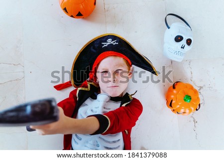Horizontal view of isolated little caucasian kid playing with Halloween pirate costume at home holding a toy ax. Seasonal and festive Halloween party concept.