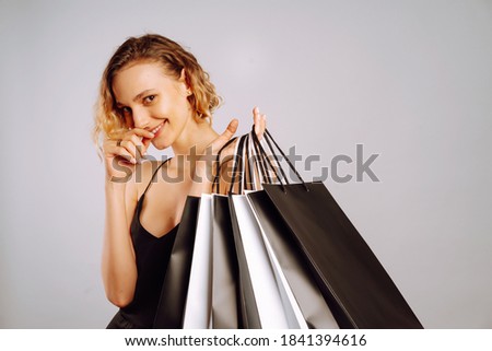 Stylish  woman after shopping posing on grey background. Young woman with black and white shopping bags. Purchases, black friday, discounts, sale concept.