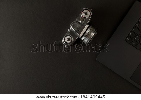 Retro analog SLR camera next to laptop on black desk in office, digital photography or image processing concept, top view flat lay from above with copy space