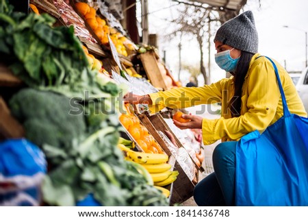 Stock photo of young woman wearing face mask buying fruit in greengrocer's shop.