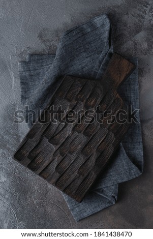 empty black wooden cutting board on a gray and blue cement or stucco background. creative template with tablecloth for copy space, top view