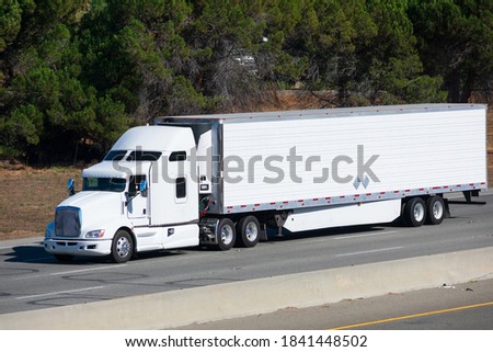 White big rig long haul semi truck transporting commercial cargo in refrigerator semi truck running alone on the eight lanes highway Royalty-Free Stock Photo #1841448502