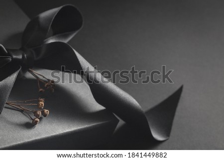 Black gift box on a dark background, decorated with a textured bow and twigs. Luxuryand elegant present for birthday, anniversary.

