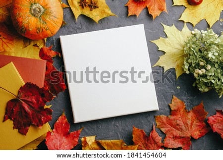 Autumn background with blank canvas board, books, pumpkin and colourful maple leaves. Mockup poster, autumn concept. Top view.