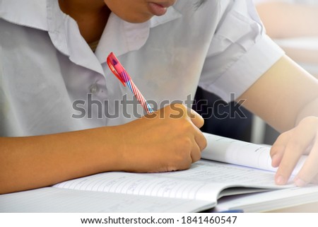Front view of Asian student holding a pen in hand and doing the test in classroon. Concept for testing, writing and doing assignment and homework. Selective focus on hand and pen.