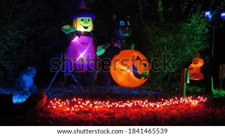 Inflatable witch with black cat and pumpkin next to country road with glowing orange lights at night Royalty-Free Stock Photo #1841465539