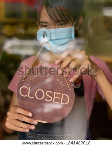 Close up shot of woman wearing mask and hand turning closed sign board on glass door in coffee shop and restaurant after coronavirus lockdown quarantine.Business crisis concept.


