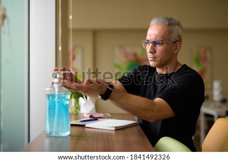 Handsome Persian man with gray hair using hand sanitizer at the library