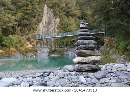 A fabulous photo of multiple level rock tower on a rock shore with a background of a bridge crossing over an emerald lake