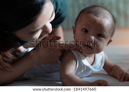 Cute asian baby girl lying on the stomach in the bed and playing with mother to relax together in bedroom before bedtime in the night.