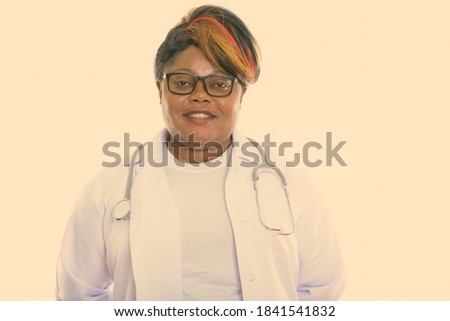 Studio shot of happy fat black African woman doctor smiling while wearing eyeglasses and stethoscope around neck