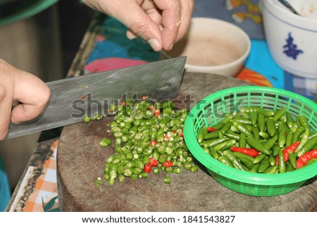 A cook cutting red and green peppers on a wooden cutting board for cooking in a restaurant on a roadside in the countryside of Thailand.