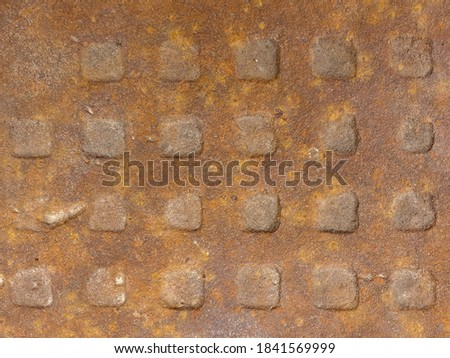 Old rusty metal plate with a pattern of square knobs.
