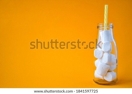 Glass cup bottle with marshmallows on a yellow background. Creative concept. Copy space.