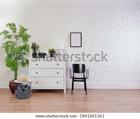 Modern white cabinet with black decorative chair, vase of plant and frame in front of the brick wall background.