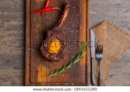 Barbecue tomahawk steak with spices served on a rustic wooden board over wooden background. BBQ concept, grilled meat steak, autumn seasonal dish.