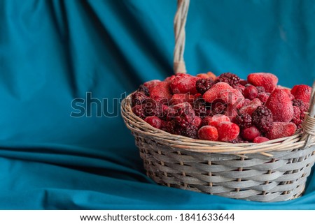 Selected focuse of Frozen berry in a wicker basket.  Mix: cherries, currants, blackberries, strawberries on a blue and beige textile background.