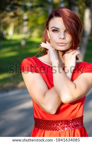 Young girl in a red dress and with evening make-up in an autumn park