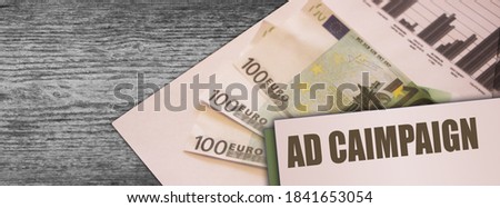 Ad Campaign words on card put on some 100 Euro banknotes on old wooden table. marketing advertising targeting business concept.